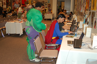 Two men gather round a computer in the press room at south by southwest, one dressed as superman, one as the incredible hulk