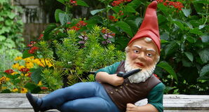 A garden gnome depicted stretched out across picnic table... with a pipe in one hand while the other props him up. Has a confrontational look in his eye...