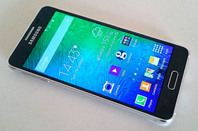 The SAMSUNG GALAXY ALPHA lies on a white background, displays Home screen icons.