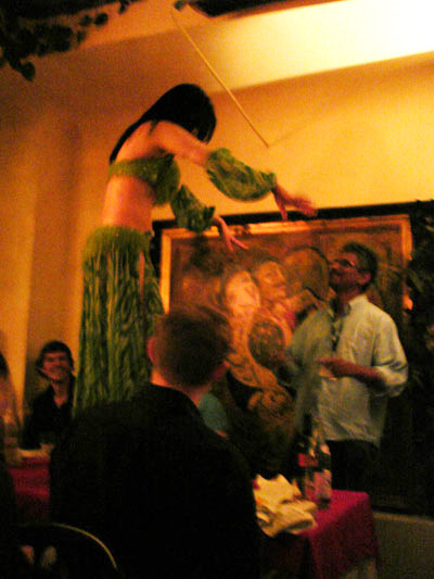 Belly dancer on table in Tunis restaurant. Three men are watching. Two are sitting down. One man is standing