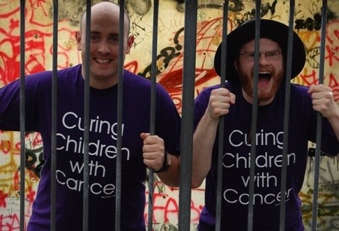 Dave Wood and Simon Painter wearing purple t-shirts with kidscan message, behind prison bars.