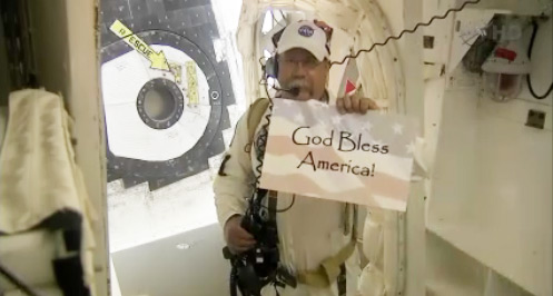 Closeout crew member before the Atlantis launch with sign reading God Bless America. Pic: NASA TV