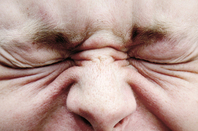 Man wrinkles his eyes in an expression of pain, annoyance or dsicomfort