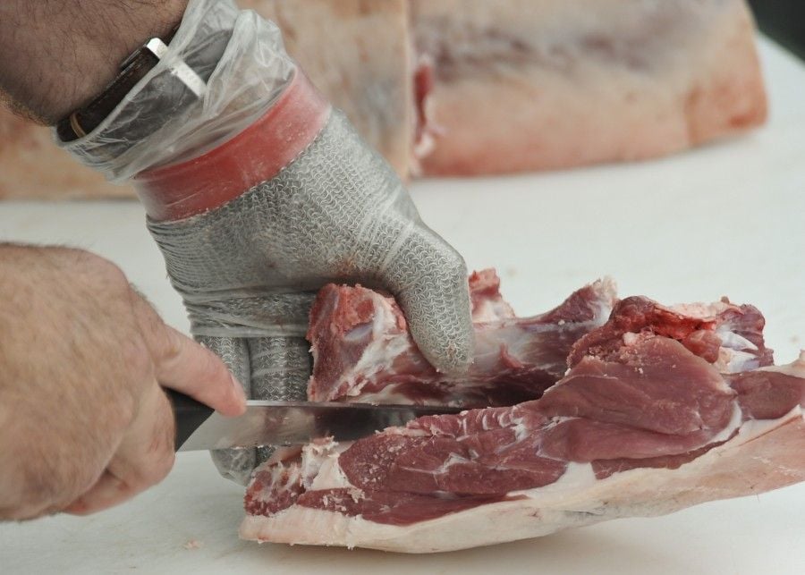 hand in chain mail glove cutting meat with sharp knife