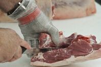 hand in chain mail glove cutting meat with sharp knife