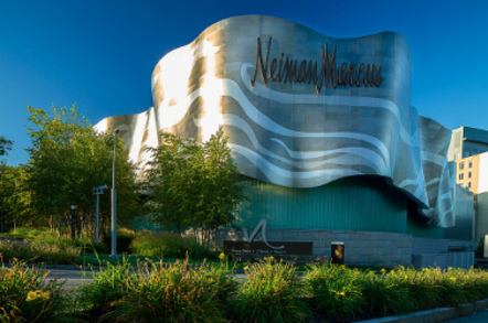 Neiman Marcus Massachusetts HQ: pearlescent gold and silver building surrounded by lush plants against a blue sky.