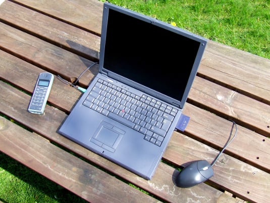 Laptop on a picnic table outside, green grass in background