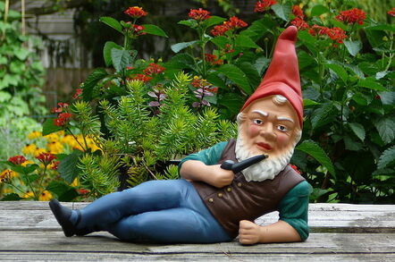 A garden gnome depicted stretched out across picnic table... with a pipe in one hand while the other props him up. Has a confrontational look in his eye...