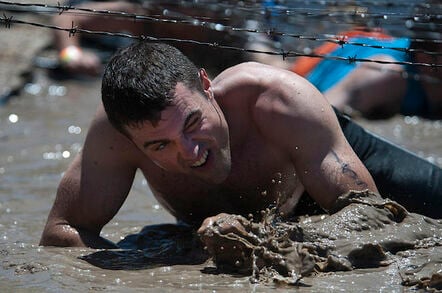 US Navy man crawling under barbed wire in tough mudder competition