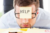 man sinks face onto pile of papers... has yellow sticky note reading help on forehead