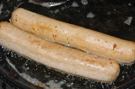 Two bratwurst frying in the pan