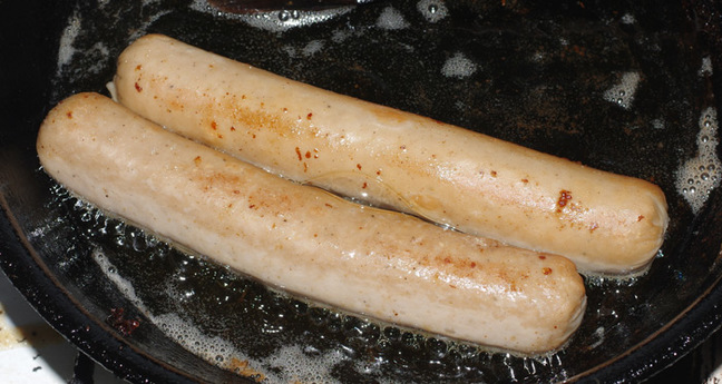 Two bratwurst frying in the pan