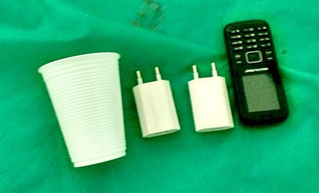 The mobile phone and chargers, shown with a plastic cup for scale