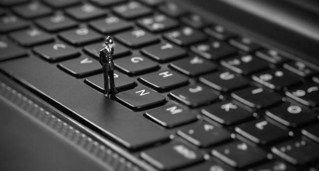 Tiny toy policeman inspects keyboard. Image via Shutterstock