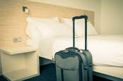 Hotel scene - suitcase propped up against freshly made bed. Image by Shutterstock