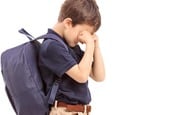 Boy with a backpack hides his eyes and cries. Pic by Shutterstock