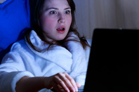 Woman in bathrobe is shocked by something she is reading on her laptop. Pic via Shutterstock