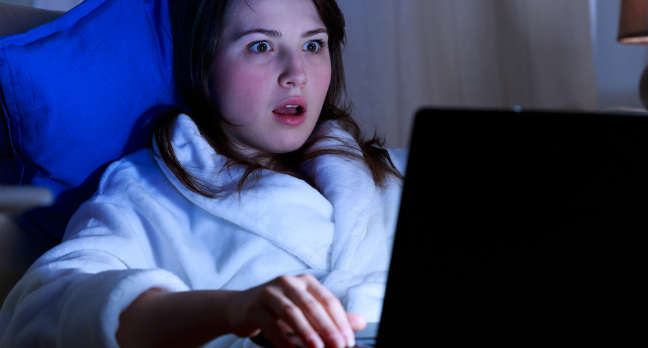 Woman in bathrobe is shocked by something she is reading on her laptop. Pic via Shutterstock