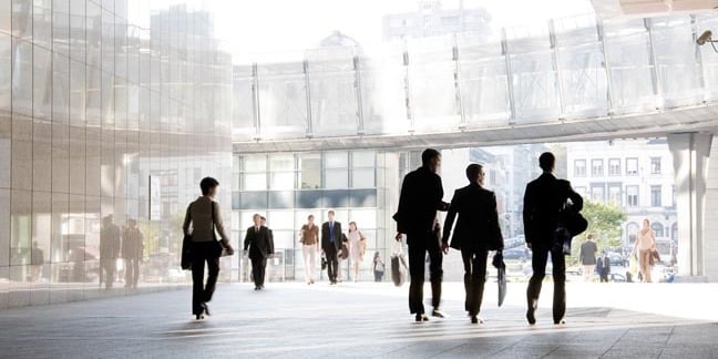 Business types walk around in a city centre square. Photo by Shutterstock