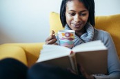 Woman reads book, sips tea on couch. Photo by Shutterstock