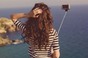 Woman takes selfie at cliff's edge with water in background. Photo via Shutterstock