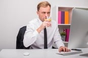 Man types something into Mac while sipping a glass of lemon water. Not a brilliant idea. Photo by SHutterstock