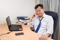 Exhausted looking business man on phone in from of laptop. Photo by Shutterstock