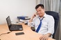 Exhausted looking business man on phone in from of laptop. Photo by Shutterstock