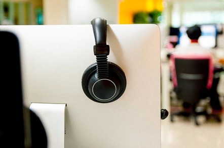 Man sits at workstation while the nuext cubicle remains empty, with the headphones hung up on the cubicle wall. Photo by Shutterstock