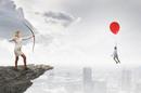 Businesswoman shoots arrow from cliff at balloon holding up rival... Bit silly conceptual art. Photo by Shutterstock