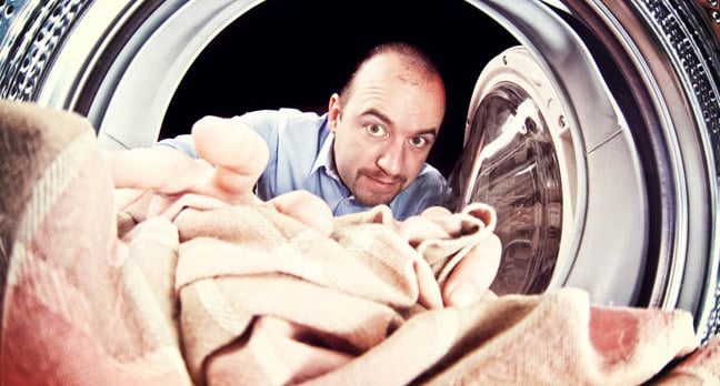 Man loads in blanket into the washing machine. Photo by Shutterstock