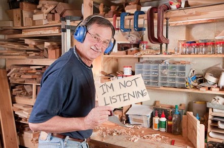 Man in woodworking workshop wearing headphones raises sign that reads "I'm not listening". Photo by Shutterstock