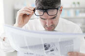 Man reading newspaper with glasses on his head 