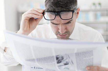 Man reading newspaper with glasses on his head