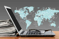 Laptop leaning against a stack of news papers in front of a world map illustration
