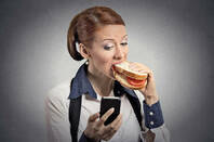 Lady eating a sandwich checking her mobile phone