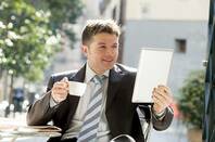 Man in a suit drinking tea out doors reading from his tablet 