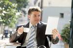 Man in a suit drinking tea out doors reading from his tablet