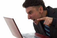 An angry man gesticulates at his laptop screen. Photo by Shutterstock