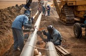 Welders wearing protective clothing fixing welding and grinding industrial construction oil and gas or water and sewerage plumbing pipeline outside on site. Photo by Andrea Slatter/Shutterstock