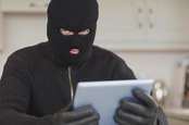 Burglar sits in kitchen with stolen tablet. Photo by Shutterstock