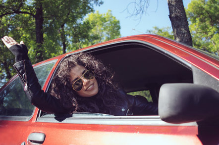 Woman motorist waves from a red car. Photo by Shutterstock