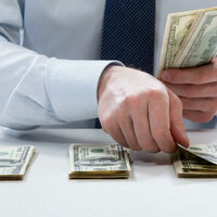Man in suit counts out piles of dollars. Photo via Shutterstock
