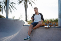 Man checks mobile while sitting on skateboard ramp. Photo by Shutterstock