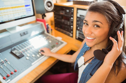 Young woman in headphones sits at mixing desk in radio/podcast studio. Photo by Shutterstock