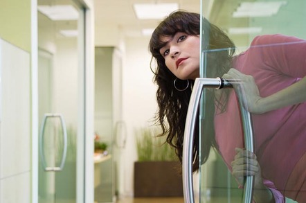 Woman looks out of office door at unseen thing/person in hallway. Photo by Shutterstock