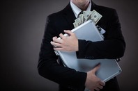 man in suit clutches briefcase full of cash. Photo by Shutterstock