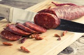 Sharp knife slices at a salami as previously sliced pieces lay on the chopping board. Photo by Shutterstock