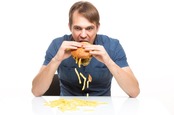 Man sloppily eats a hamburger... chips and pickle fall out. Photo by Shutterstock