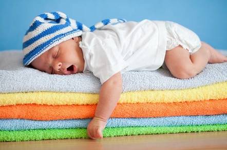 Yawning sleeping baby on colourful stack of towels